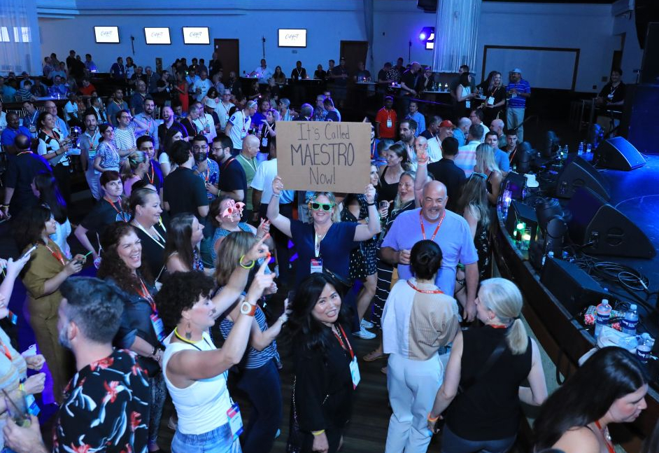 At the Flo Rida concert, a woman in the center of the crowd holds up a handwritten sign reading "It's called Maestro now!"