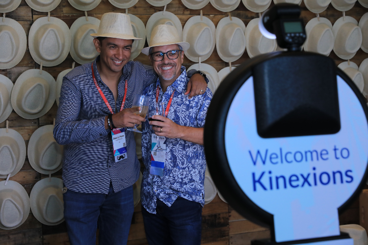 Two male attendees try on panama hats for a photo op booth at Kinexions. 