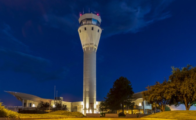 A control tower at an airport is lit up against the night sky.