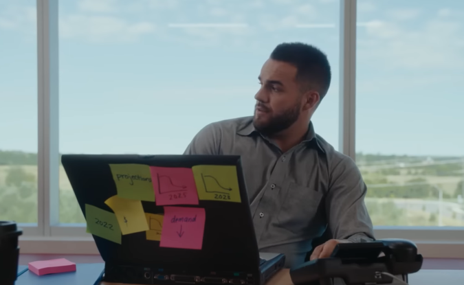 Supply chain planner sits at a desk with a laptop covered in sticky notes that indicate demand and supply trends.