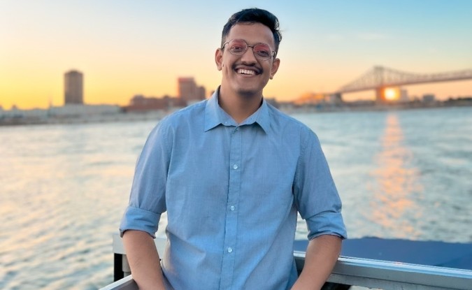 Kinaxis intern Kevin Jivani stands on a boat with his back to a sunset over a distant city and bridge