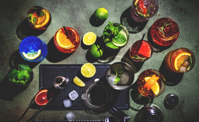 An assortment of mocktails are arranged on a countertop, surrounded by mint, limes and other ingredients.