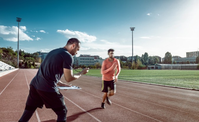 Runner and coach training on track and field. The coach is measuring results with a stopwatch.